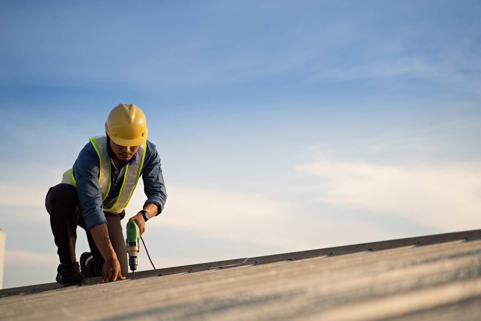 Worker repairing the roof on a construction site. Electric drill used on roof, Roof construction concept.